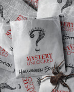 White envelope with 'Mystery Unlocked' text on a Halloween-themed background with spider webs and a spider.