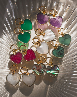 A collection of heart-shaped interchangeable earring charms in various colors like red, green, purple, and pink, attached to small gold-colored hoop earrings.