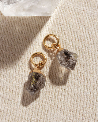 Two hoop earring charms with large Herkimer quartz gems attached to small gold-colored hoop earrings, placed on a textured fabric.