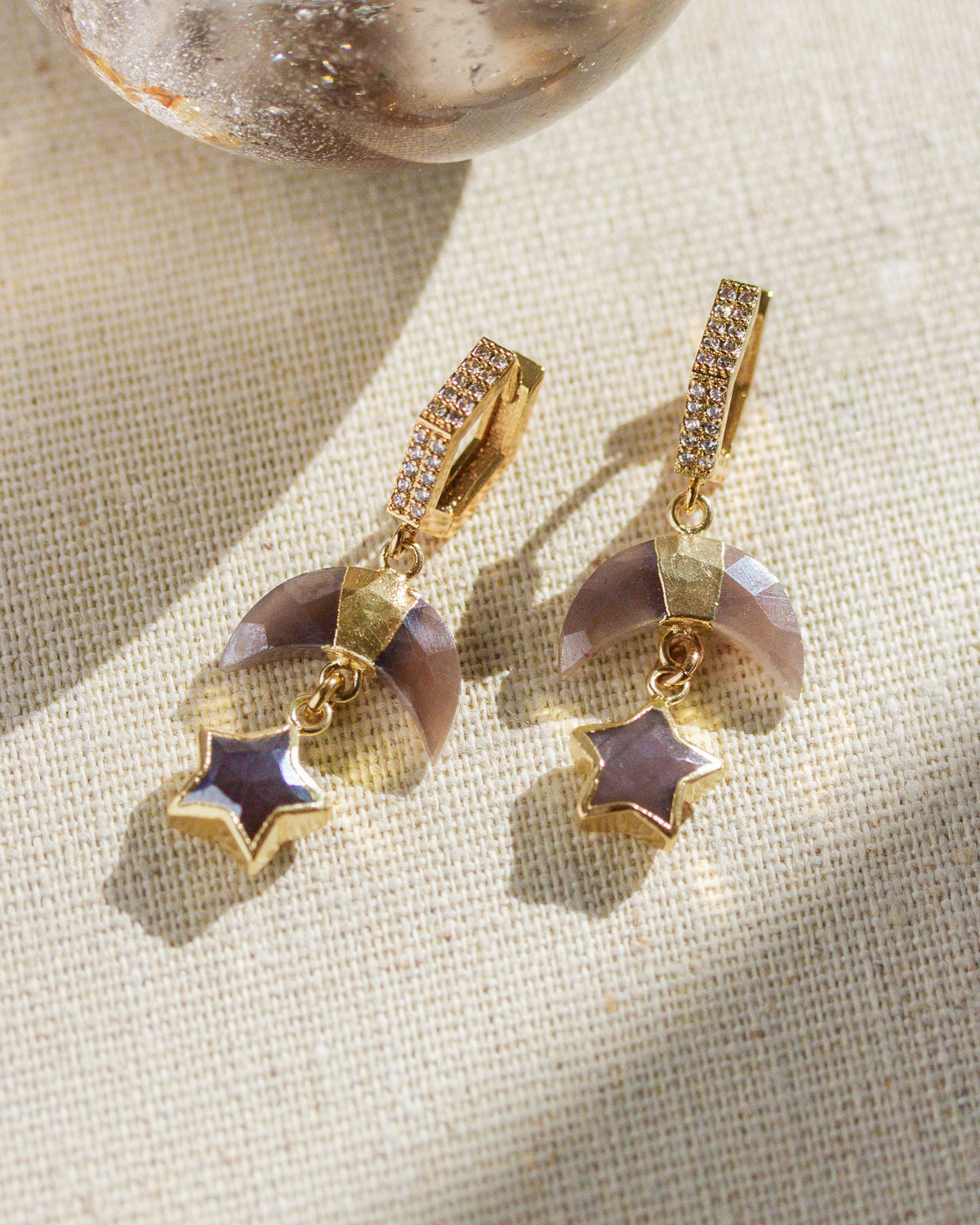 Coffee moonstone and cz moon, star, hoop earrings on a textured white surface.