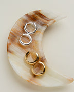 Two pairs of gold hoop and silver hoop earrings on a crescent moon calcite dish.