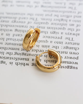 Minimal gold plated huggie hoop earrings laying on a book page.