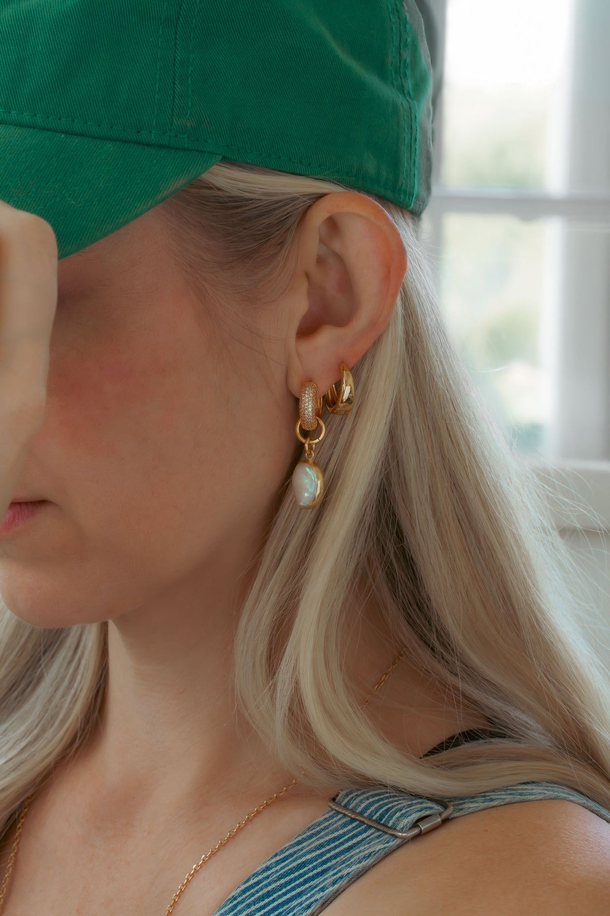Close-up of a person wearing a green cap and gold earrings pearl charms with a blurred background