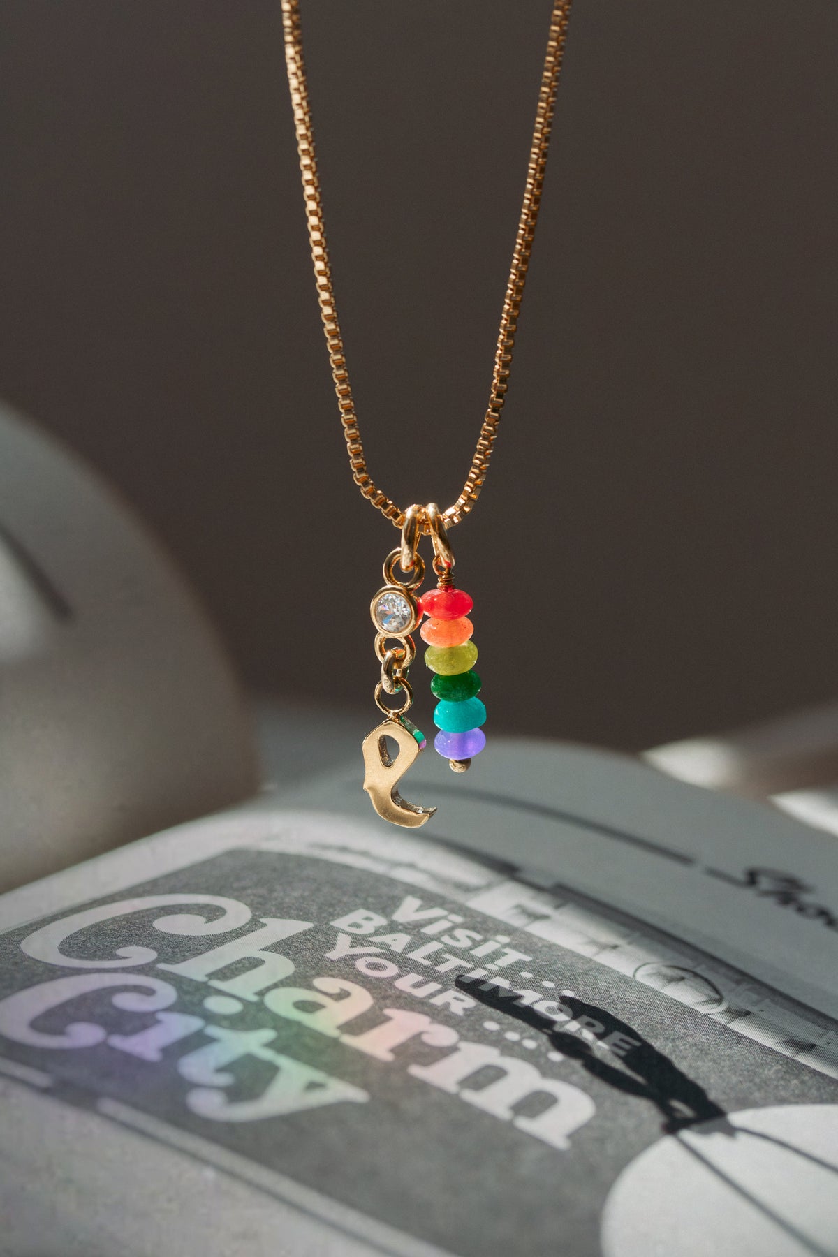 Gold initial necklace with rainbow charm on a newspaper background