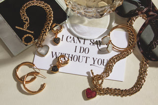 Several gold toggle heart necklaces and earrings posed next to a note that reads: "I can't say I do without you."