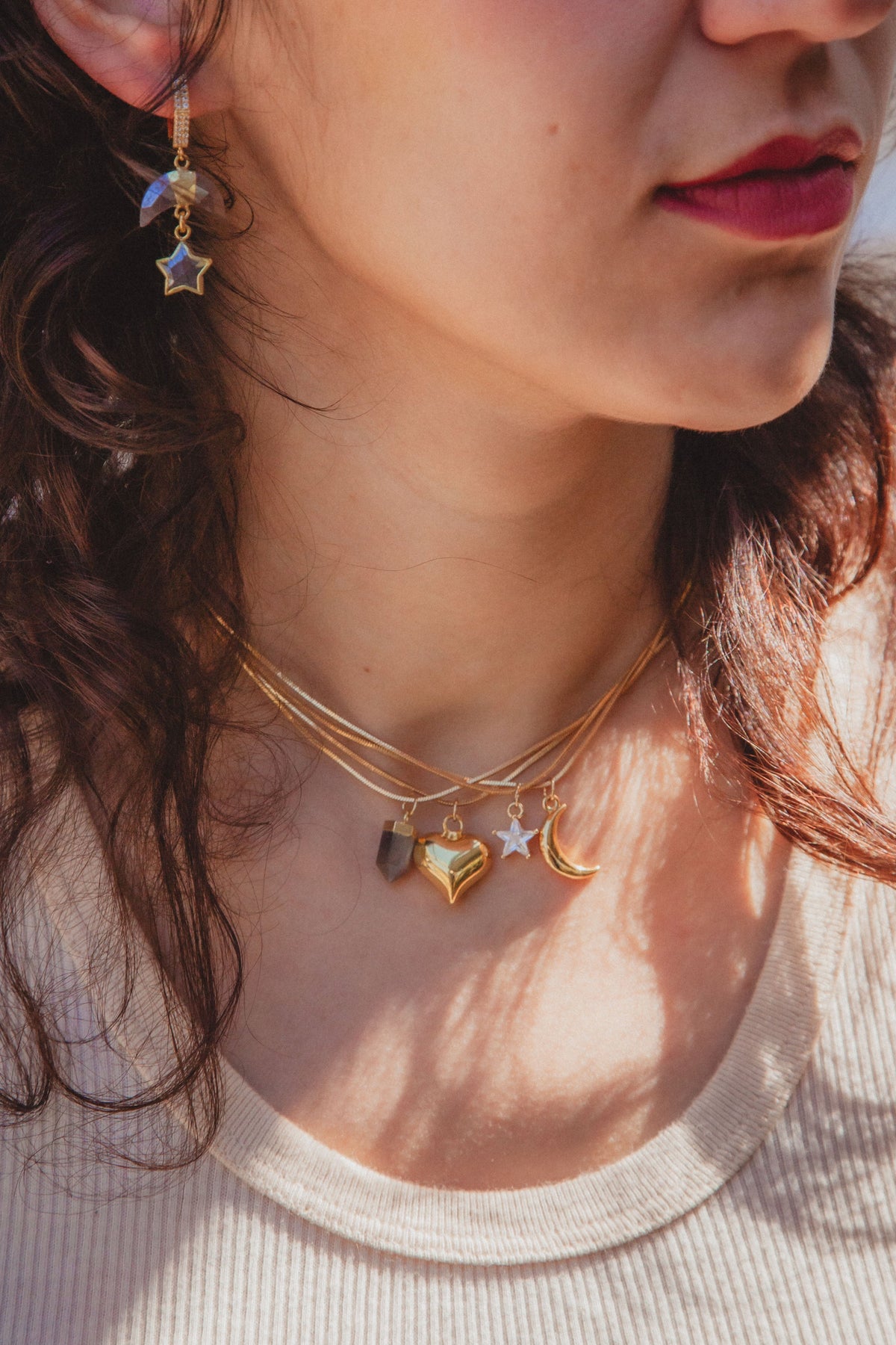 Woman wearing layering necklace with many charms and charm earrings.