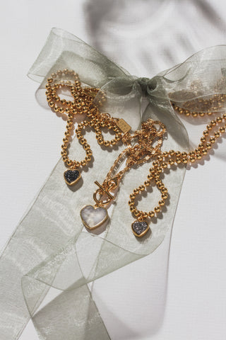 Flat lay image of several Luna Norte heart shaped necklaces laying atop a table with a semi-transparent ribbon tied on a bow.