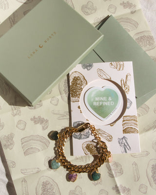 Bracelet with charms with green Luna Norte box with a card featuring 'MINE & REFINED' and gemstone illustrations wrapping paper.