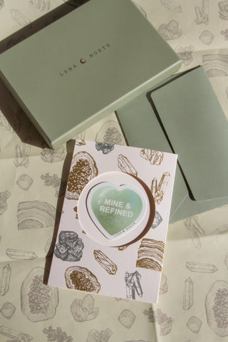 Green Luna Norte box with a card featuring 'MINE & REFINED' and gemstone illustrations wrapping paper.