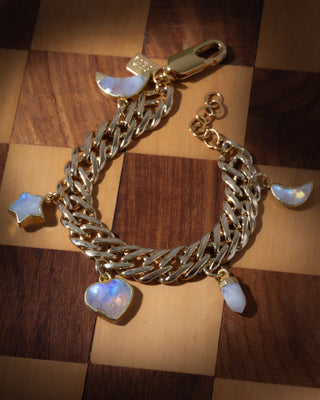 Gold chain bracelet with moonstone star, heart, and moon charms on a wooden surface.