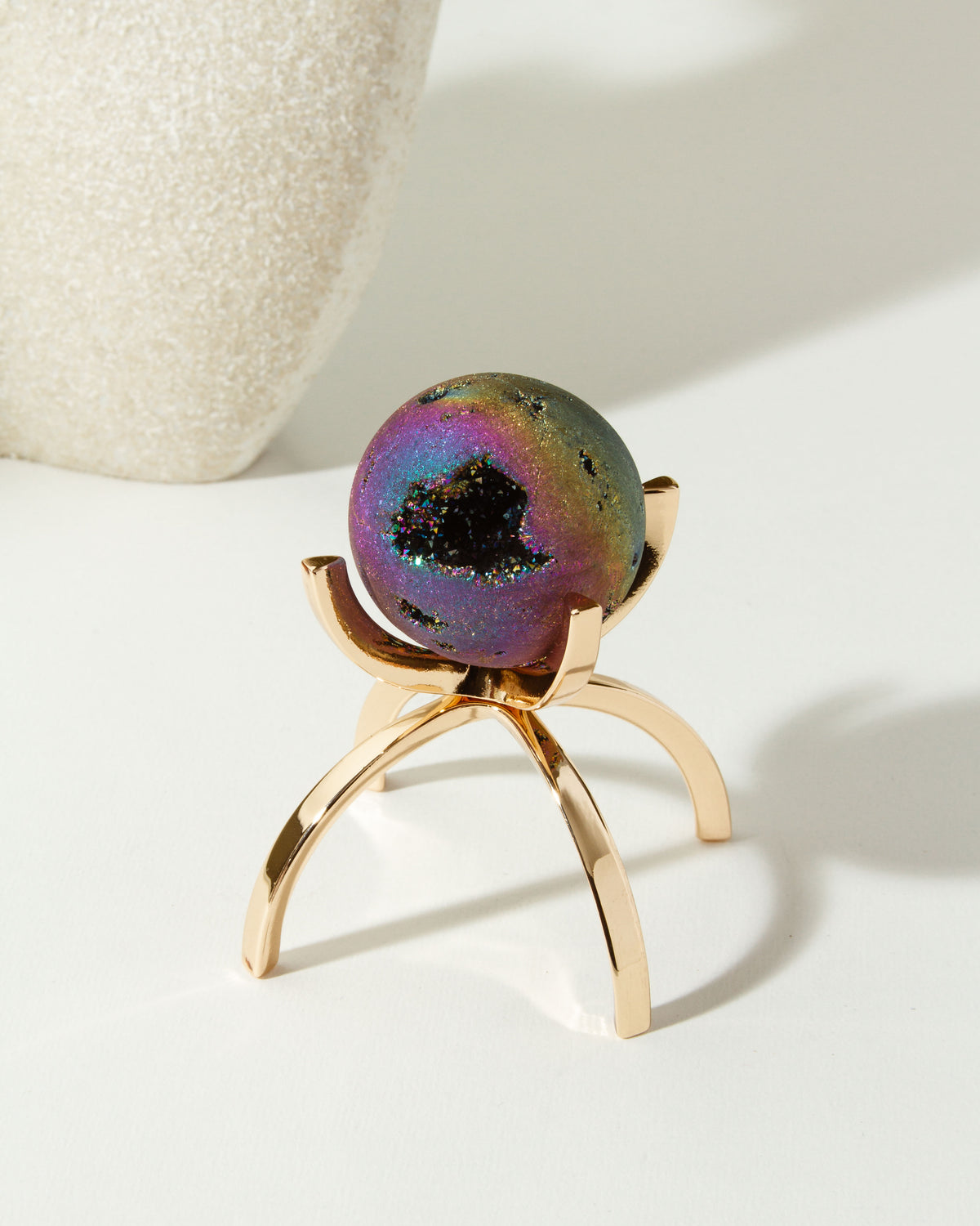 Rainbow druzy gemstone sphere on a gold stand.