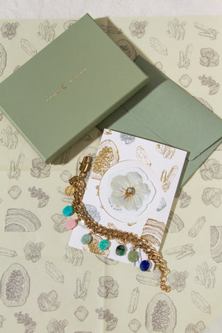 Bracelet with colorful beads on a gift card with a floral and crystal design, placed on a patterned wrapping paper.