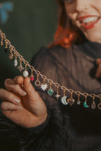 Woman holding a decorative chain with small charms against a dark background with colorful bows.