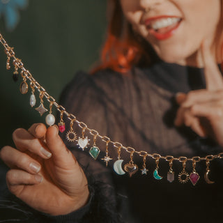 Woman holding a decorative chain with small charms against a dark background with colorful bows.