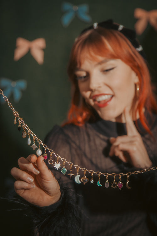 Woman holding a decorative chain with small charms against a dark background with colorful bows.