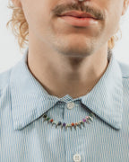 A man with curly light brown hair and a mustache wearing a colorful gemstone spike necklace.