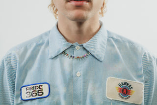 Person wearing a silver spiked necklace and blue striped shirt with 'Pride 365' logo patch