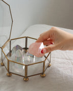 Hand placing rose quartz stone into a glass box on a white surface.