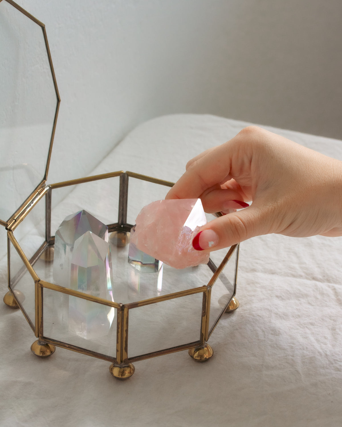 Hand placing rose quartz stone into a glass box on a white surface.