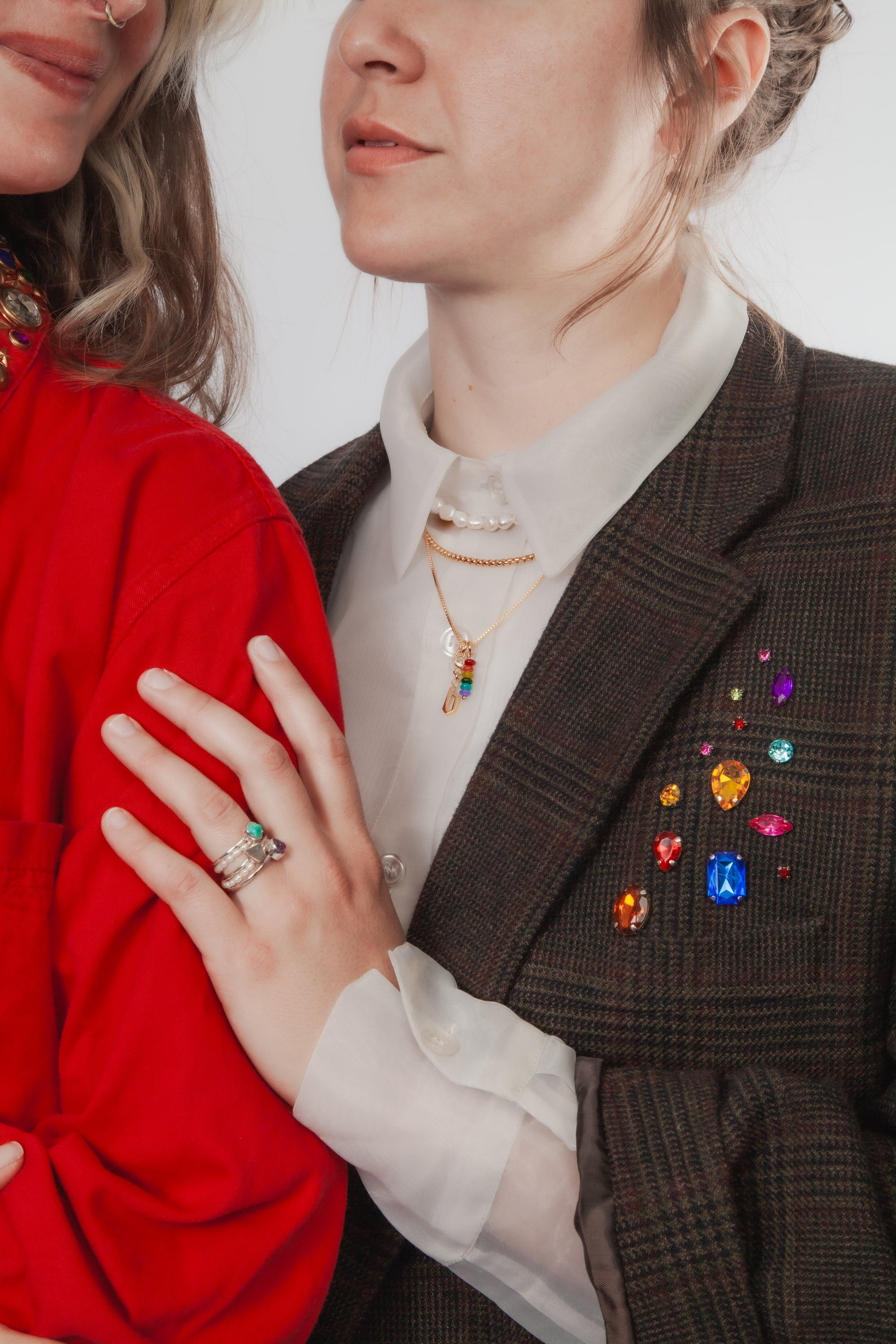 Two people wearing layered jewelry and jackets featuring colorful embellishments 