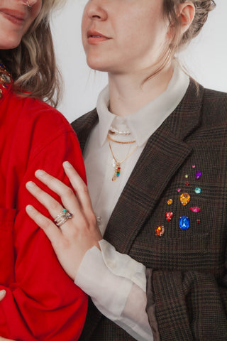 Two people wearing layered jewelry and jackets featuring colorful embellishments 