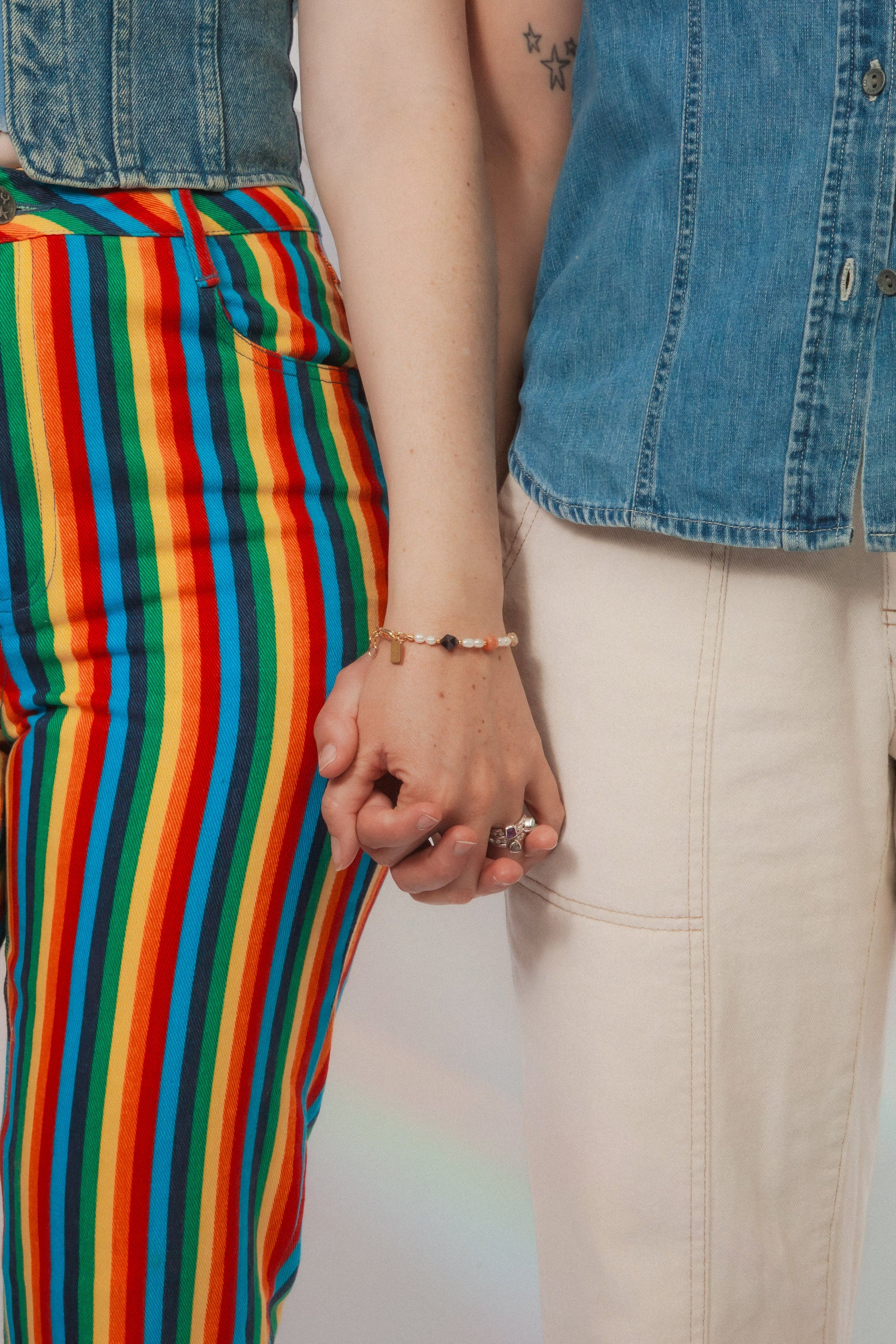 Two people wearing colorful striped pants and a denim shirt and gemstone bracelet and rings