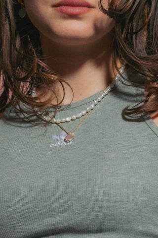 A model wearing a gray ribbed halter with white pearl beaded necklace and heart charm.