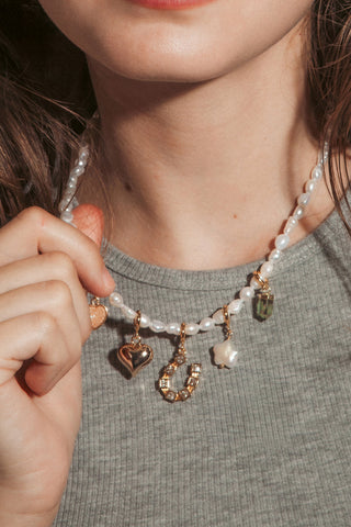 A woman with wavy brown hair wearing a pearl beaded necklace with small charms and matching sun drop earrings.