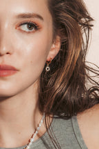 A woman with wavy brown hair wearing gold clear CZ sun charm huggie hoop earrings.