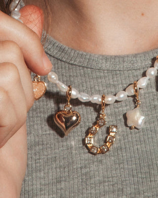 A model wearing pearl beaded necklace with puffy gold heart charm and horseshoe charms.