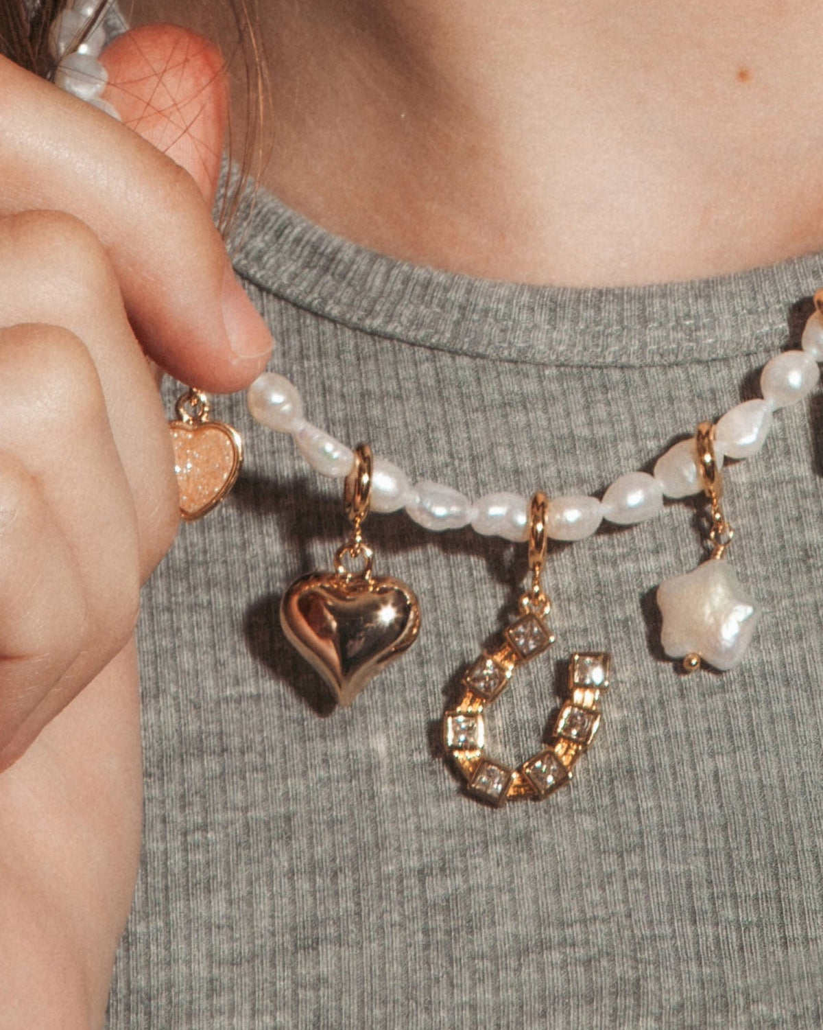A model wearing pearl beaded necklace with puffy gold heart charm and horseshoe charms.