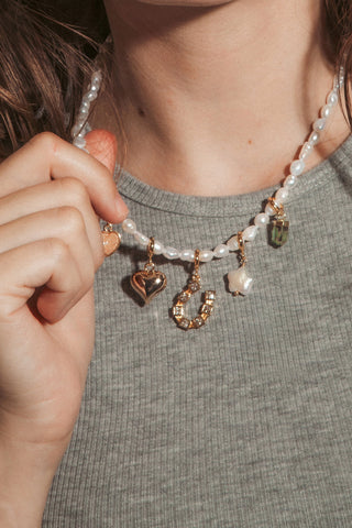 A woman with wavy brown hair wearing a pearl beaded necklace with gold charms.