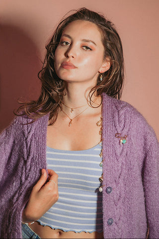 Woman wearing gold gemstone jewelry and a charm-adorned cardigan.