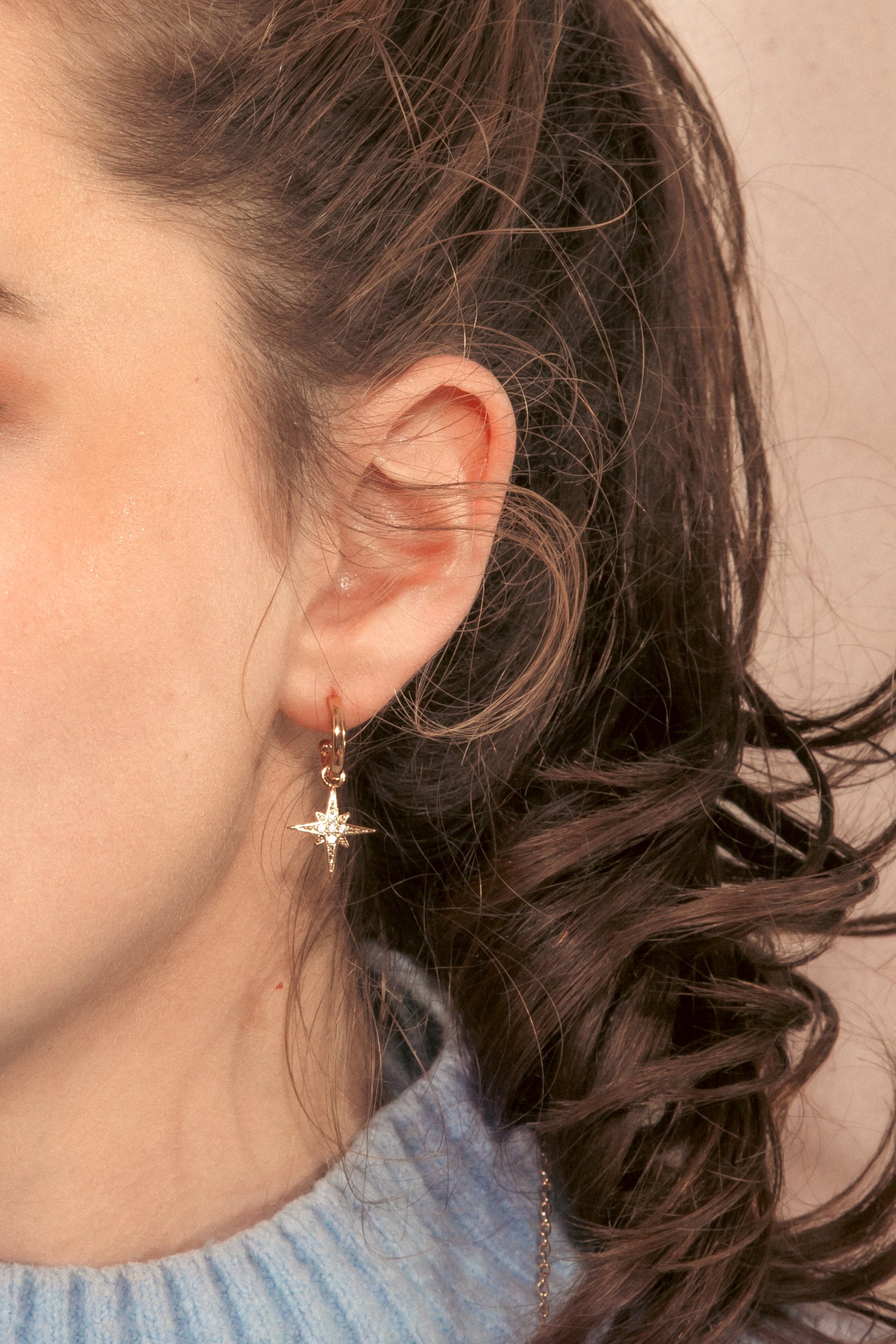 Woman with brown hair, wearing a light blue turtleneck sweater and clear CZ star gold hoop earring. 
