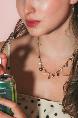 Model is wearing a cream-colored spaghetti-strap top with black polka dots and a gold beaded gemstone charm celestial necklace.