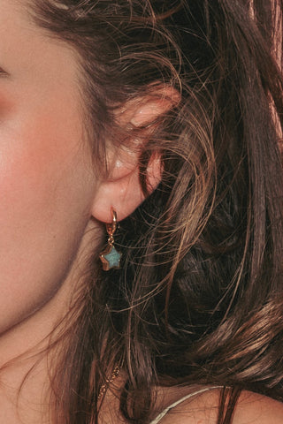 Model wearing gold and green gemstone hoop earring.