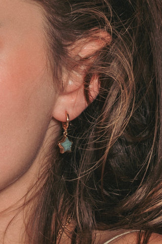 Model wearing green gemstone star huggie hoop earring.