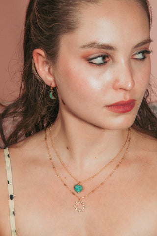 A model wearing layered gold necklaces, one with a amazonite stone pendant and another with a clear CZ charm, paired with a cream and black polka dot top.