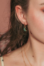 Model wearing green gemstone crescent moon huggie hoop earring.
