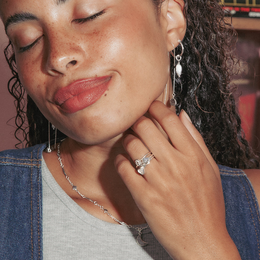 Woman wearing jewelry, featuring silver gemstone rings, a delicate silver necklace, and dangling silver earrings.