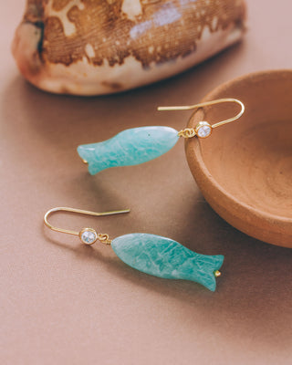 Amazonite fish-shaped earrings with gold hooks on a beige surface.