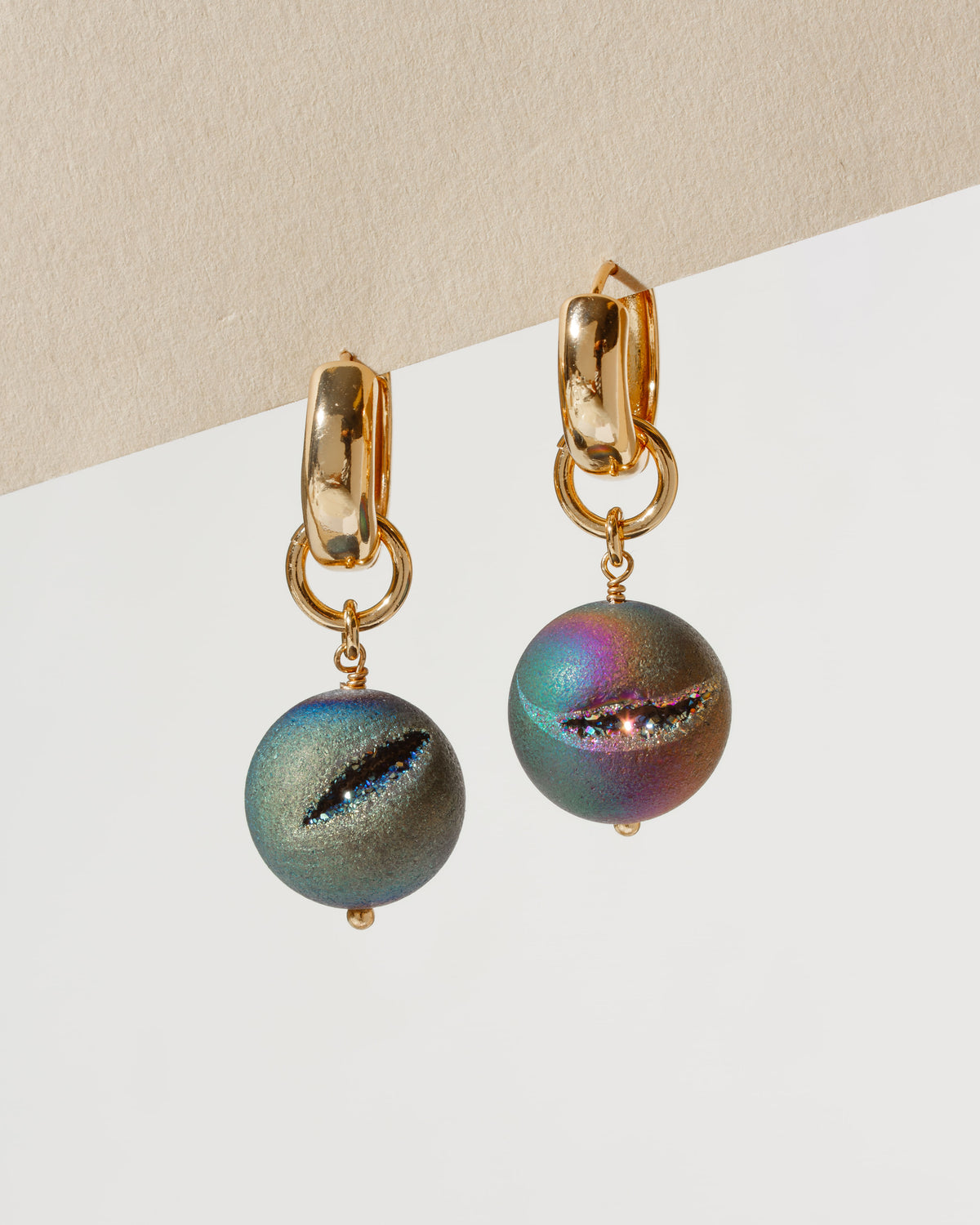 Pair of gold hoop earrings with rainbow druzy spherical charms.