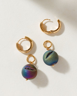 A set of gold-colored hoop earrings featuring a colorful druzy sphere bead charm attached to it, displayed on a white surface.