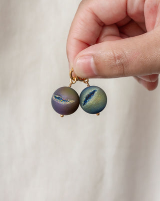 Gold interchangeable rainbow druzy spherical charms being held against a white backdrop.