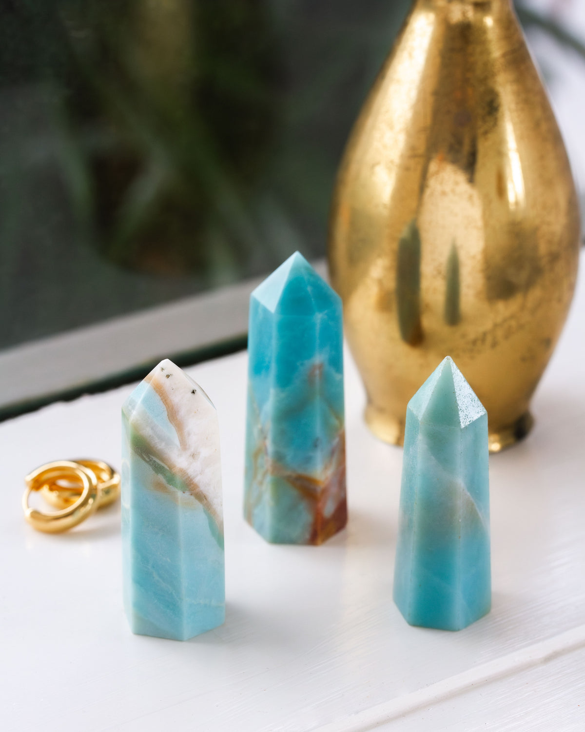 Three blue amazonite mini towers sitting on a white windowsill with bronze lamp in the background