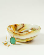 Banded calcite jewelry bowl in green, brown, and beige with a necklace over the edge