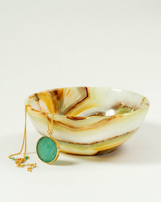 A banded calcite jewelry bowl with a necklace hanging over its edge, displaying earthy tones like greens, browns, and beige.