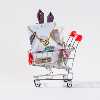 Miniature shopping cart with jewelry and packaging on a white background