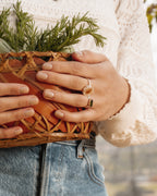 A hand holds a basket, wearing a Green Tourmaline and a Clear Quartz Kaleidoscope Ring.