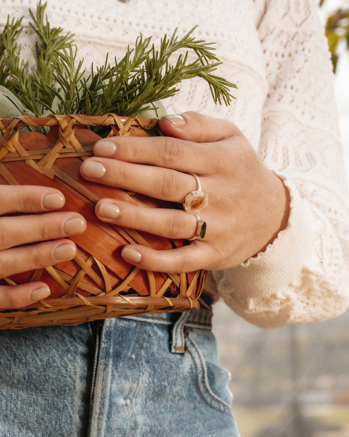 A hand holds a basket, wearing a Green Tourmaline and a Clear Quartz Kaleidoscope Ring.